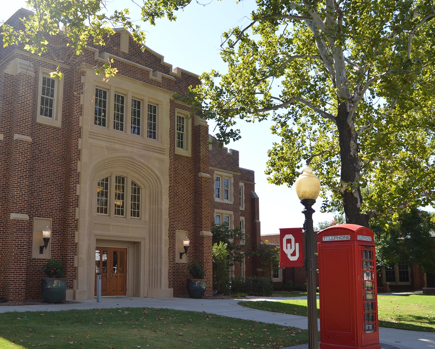 Farzaneh Hall, with trees, a lamppost with an OU flag, and a red phone booth.