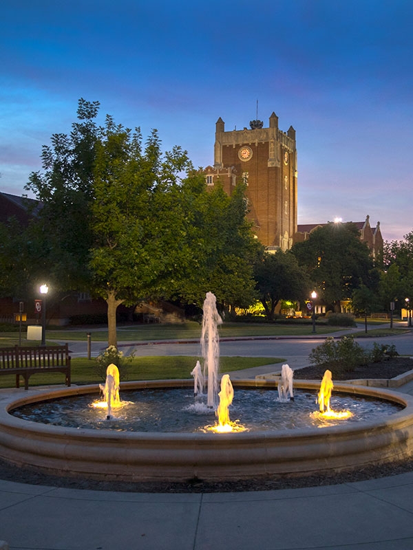 Oklahoma Memorial Union at dusk, with a fountain and trees in the foreground.