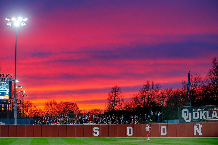 OU's Sooner softball team playing an evening game, with a pink, purple, and orange sky.