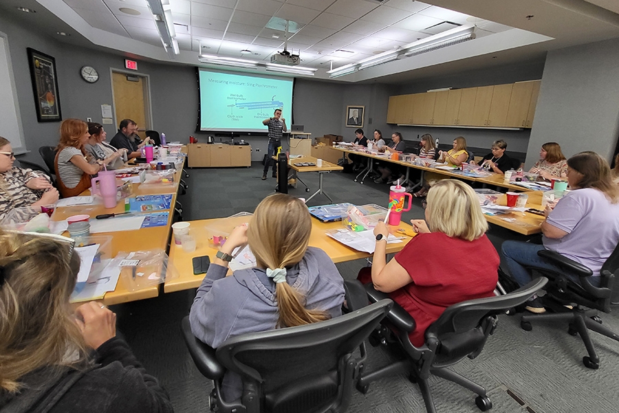 A scientist speaks to a full room of teachers sitting at tables.