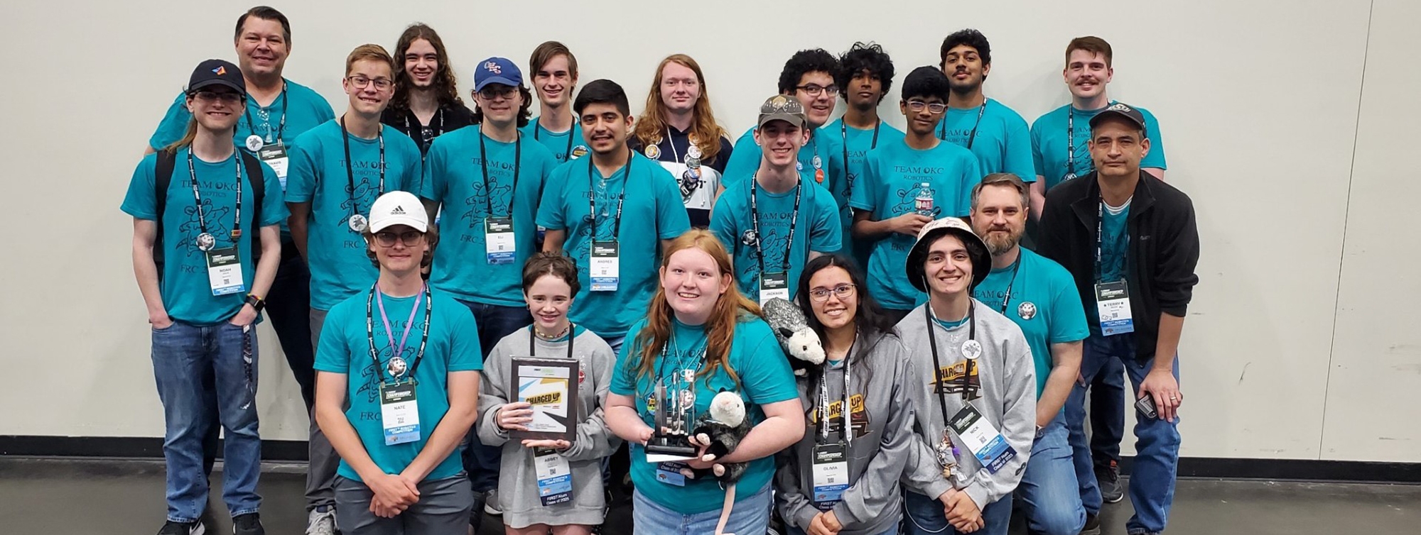 a group of teenagers and adult sponsors pose with their trophies.