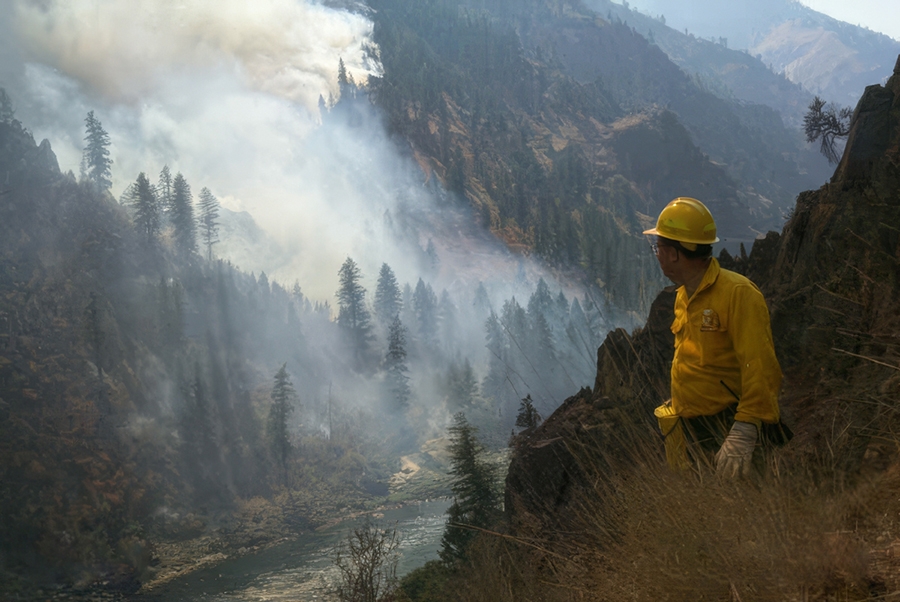A firefighter on a ridge overlooking a smokey mountain.