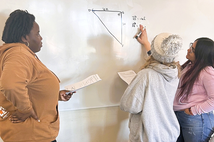 Three students working on a mathematical equation on a whiteboard.