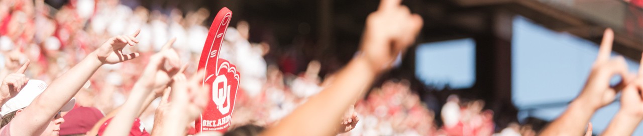 Students at a football game using the iconic "there's only one" hand gesture with a foam finger in the middle of the crowd.