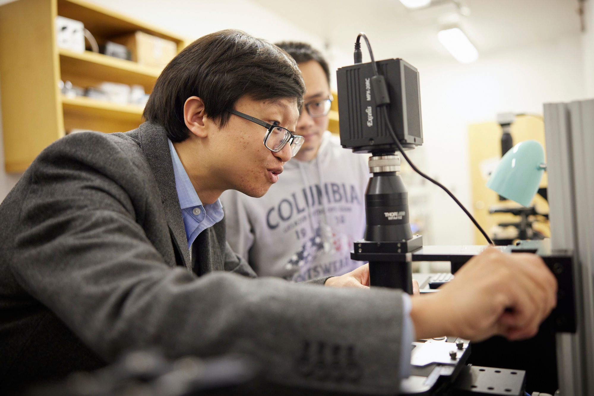 Yuchen Qui observes a piece of equipment in the biomedical engineering lab while a student looks on.