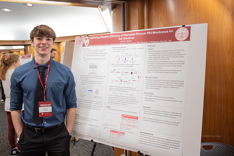 Jackson Clymer Standing next to their research poster titled "Evaluating Filtration Effficiency of Diacrylate Pluronic P84 Membranes for Salt Solutions"
