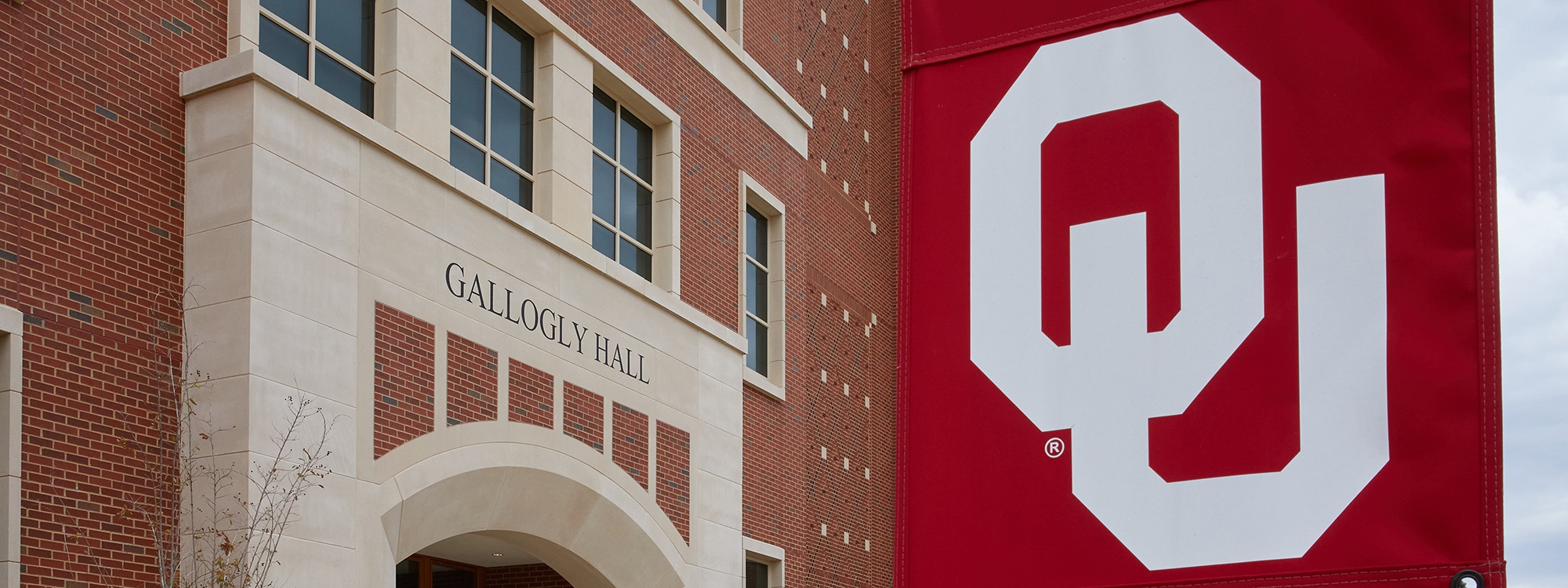 Entrance archway of Gallogly Hall with interlocking OU flag on pole.
