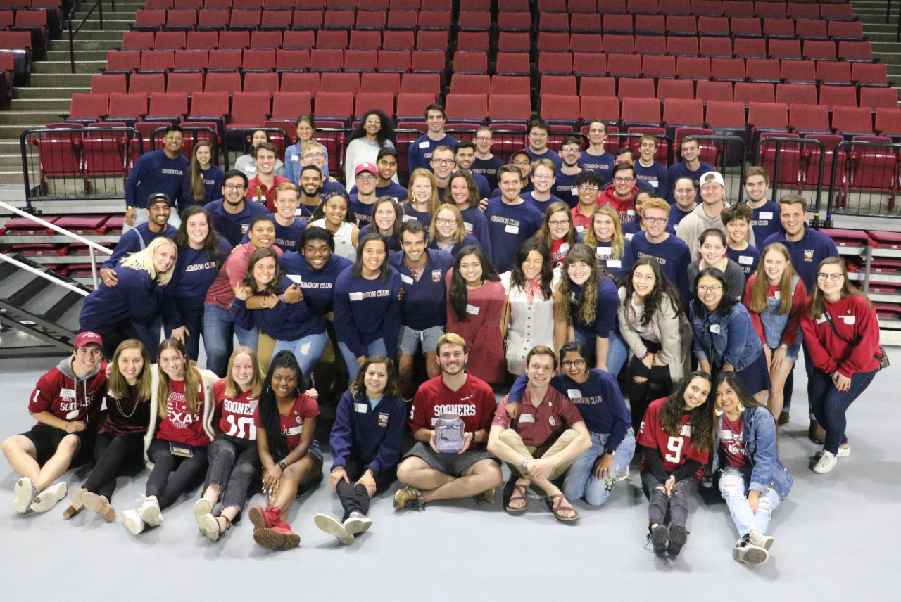 Crimson Club students sitting on the floor of the Lloyd Noble Center for a group photo.