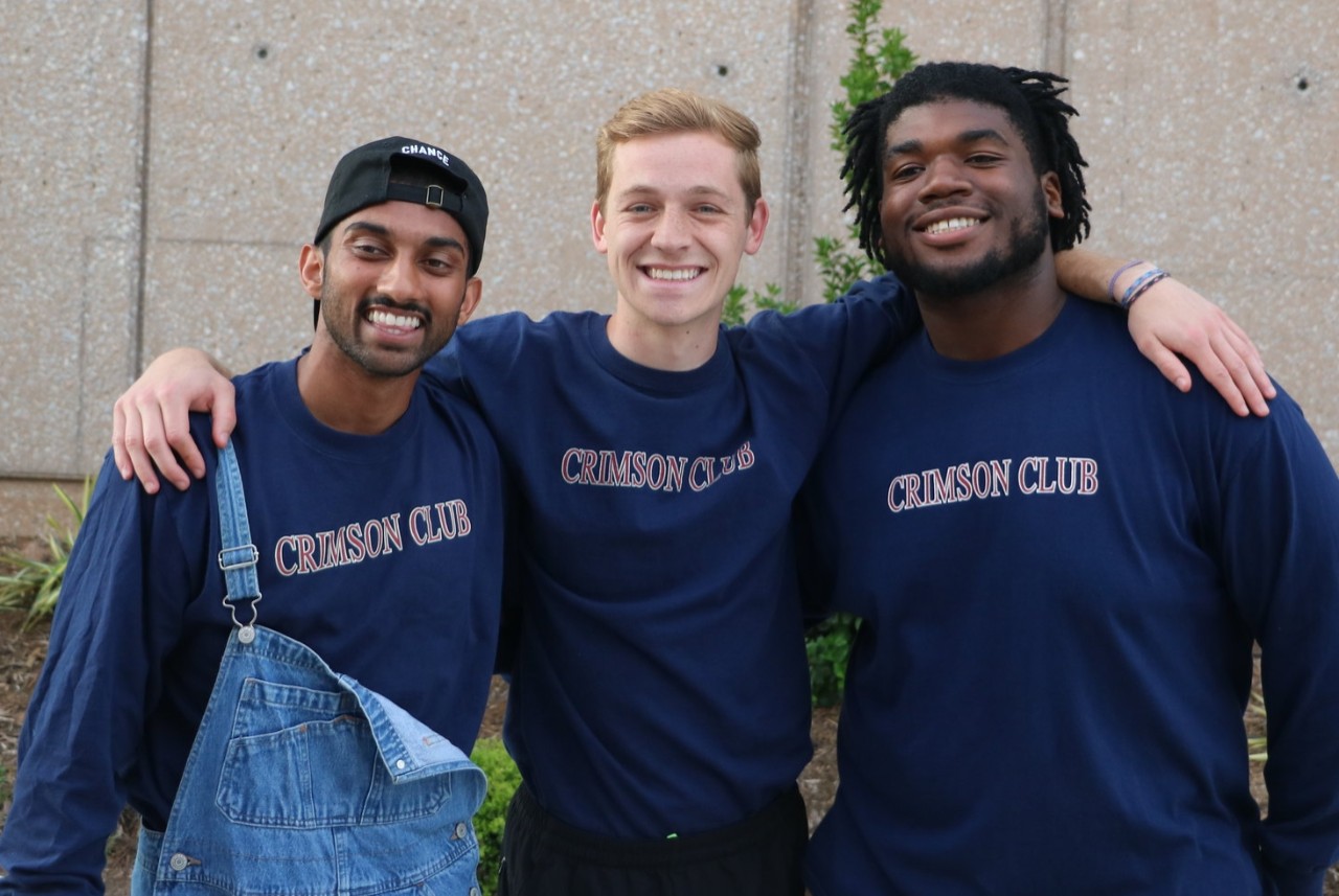 Three Crimson Club students standing with arms around one another smiling. 