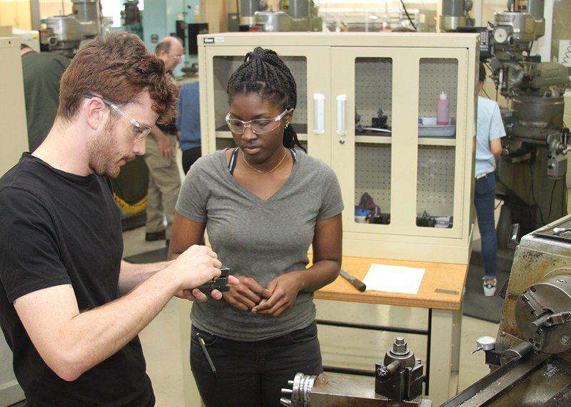 Two students wearing safety glasses looking at an object.