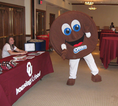 An oreo mascot posing in front of a table with a student smiling.