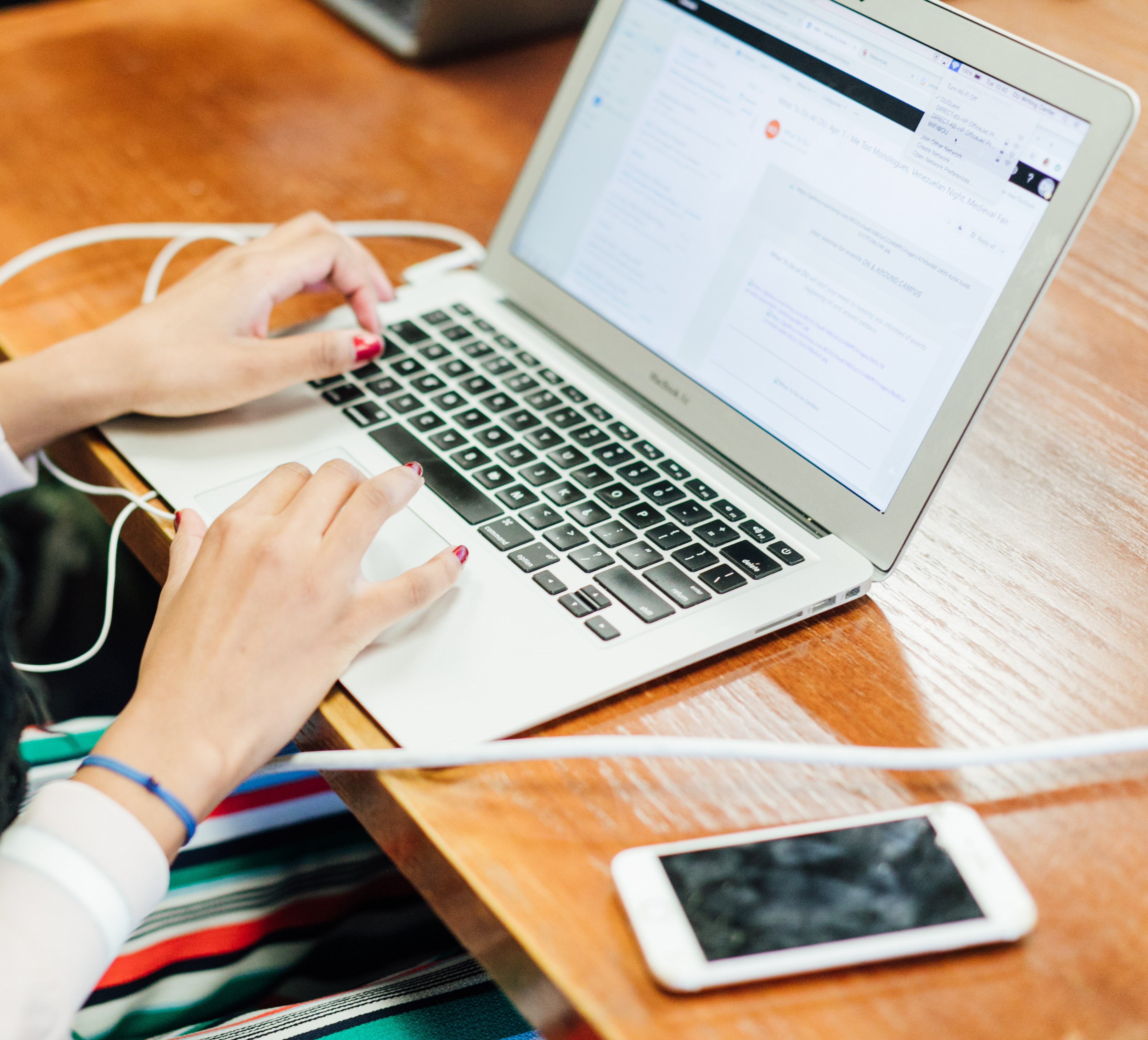 A classroom with rows of desks, where students are seated, each with name placards in front of them. Some desks have laptops and pencil cases. The students are smiling and looking toward the front of the classroom, attentively listening to the lecture or presentation.