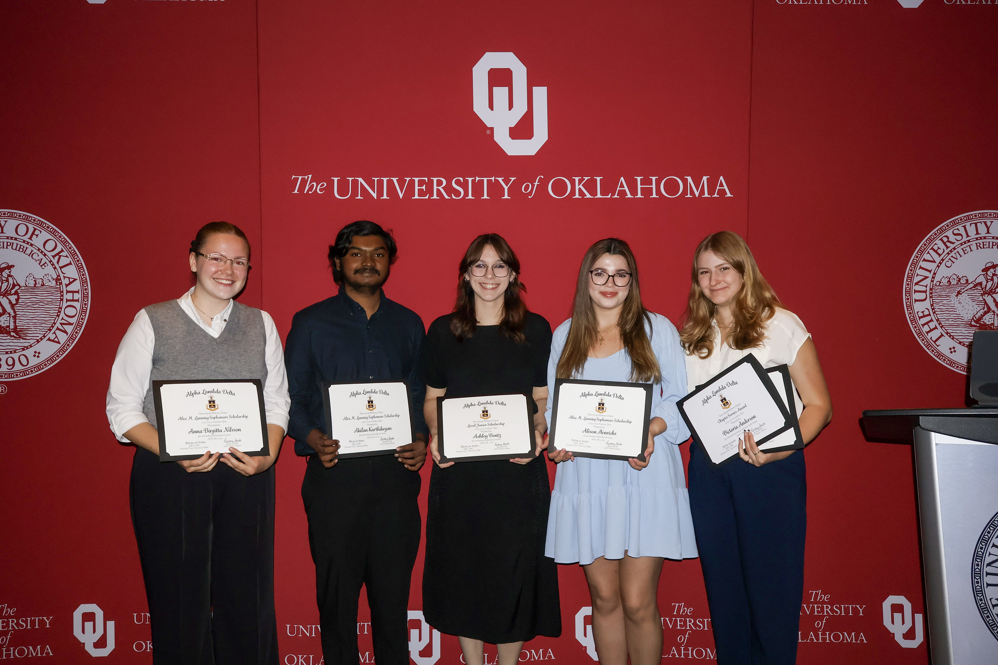 Five students holding up their awards at an award ceremony.