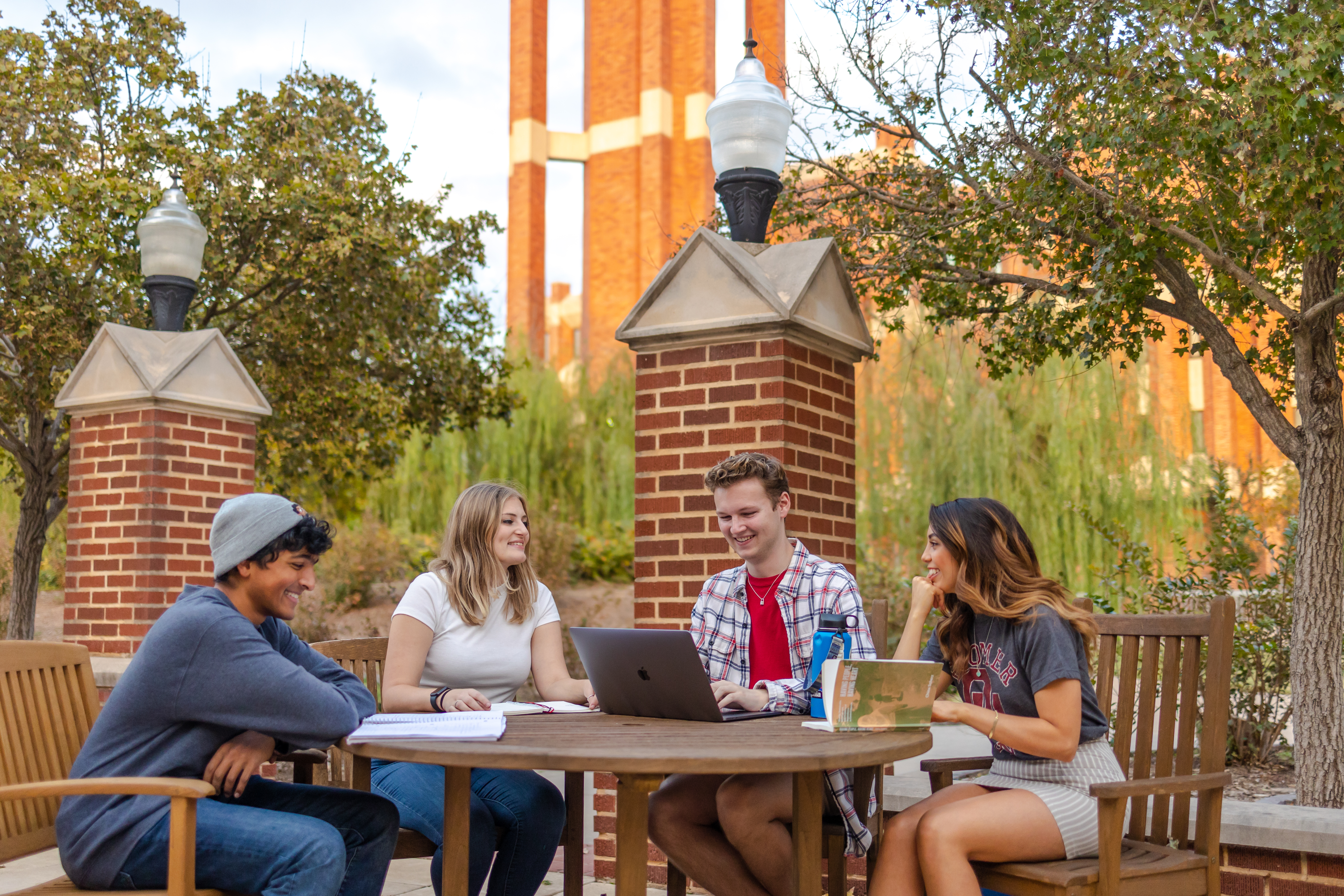 Four students studying together outside at a table with a computer