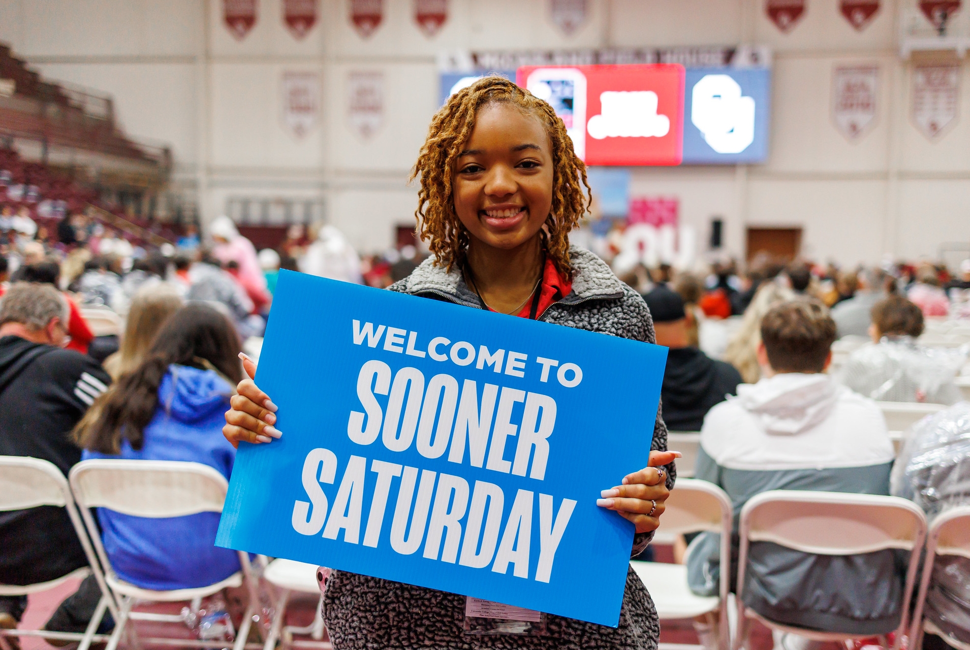 Student holding a "Welcome to Sooner Saturday" sign 