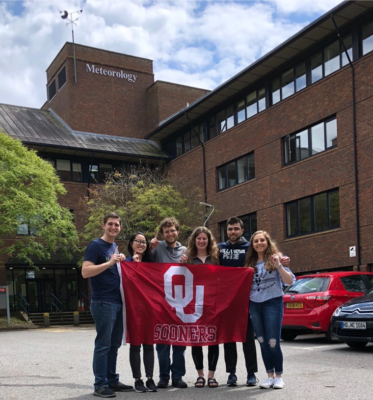 Six Students infront of the Reading University's Meterology building, holding a red flag that says OU Sooners