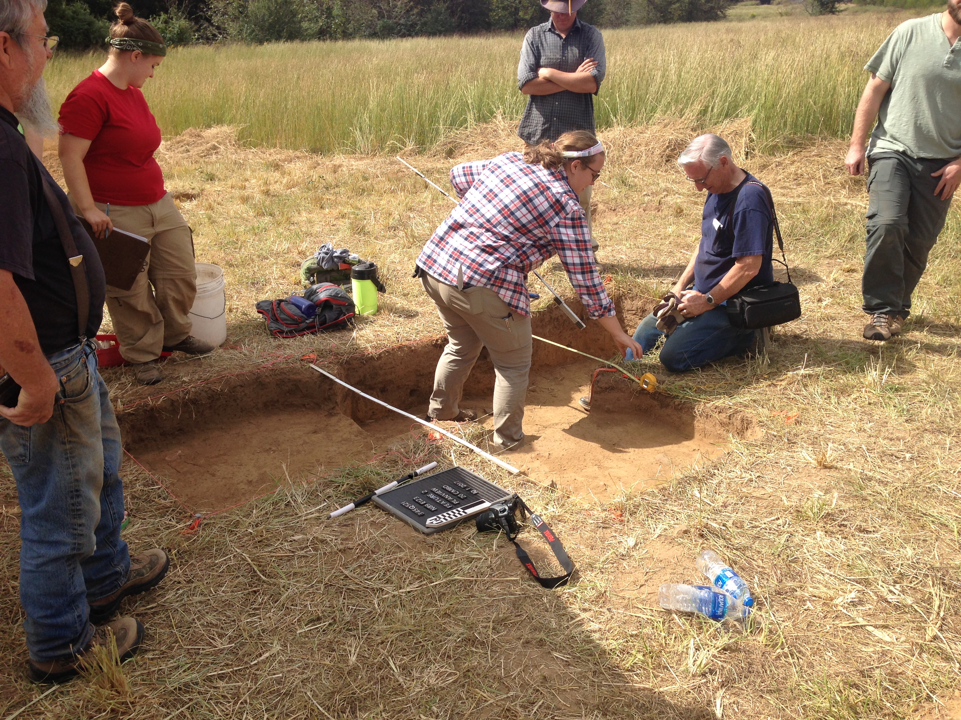 People digging in a grassy area with simple digging equipment.