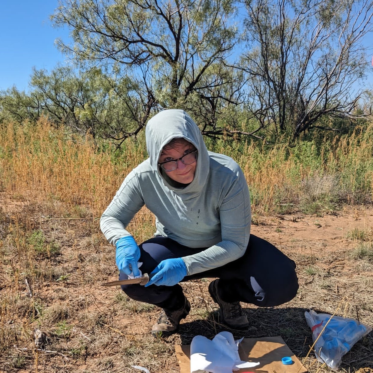 Photo of Kieran Carroll outside with a small shovel and test tubes on the ground.