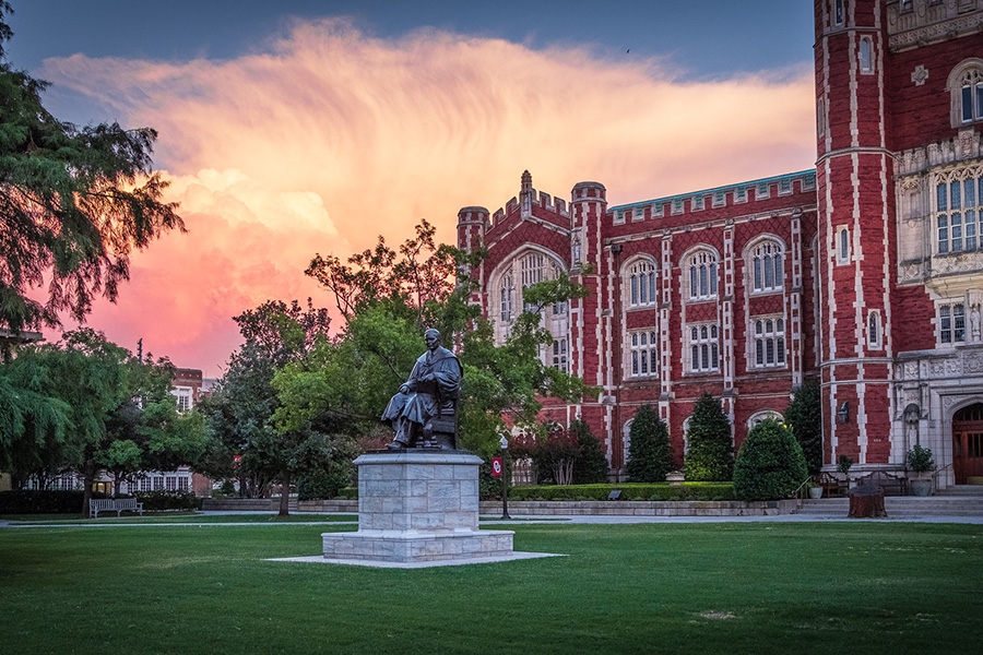 A thunderstorm forming behind Evans Hall at sunset, with a statue in the foreground.