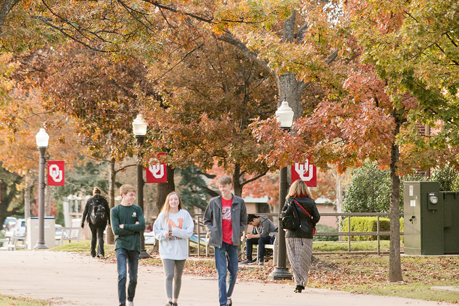 Students walk on the oval on the Norman campus framed by fall colors.