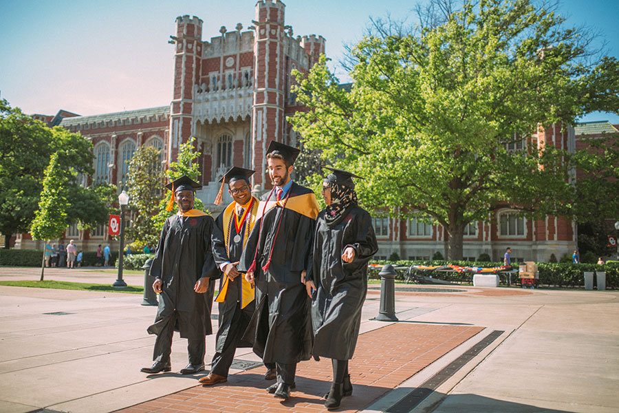 A group of graduates in their regalia giving the 'one OU' sign.