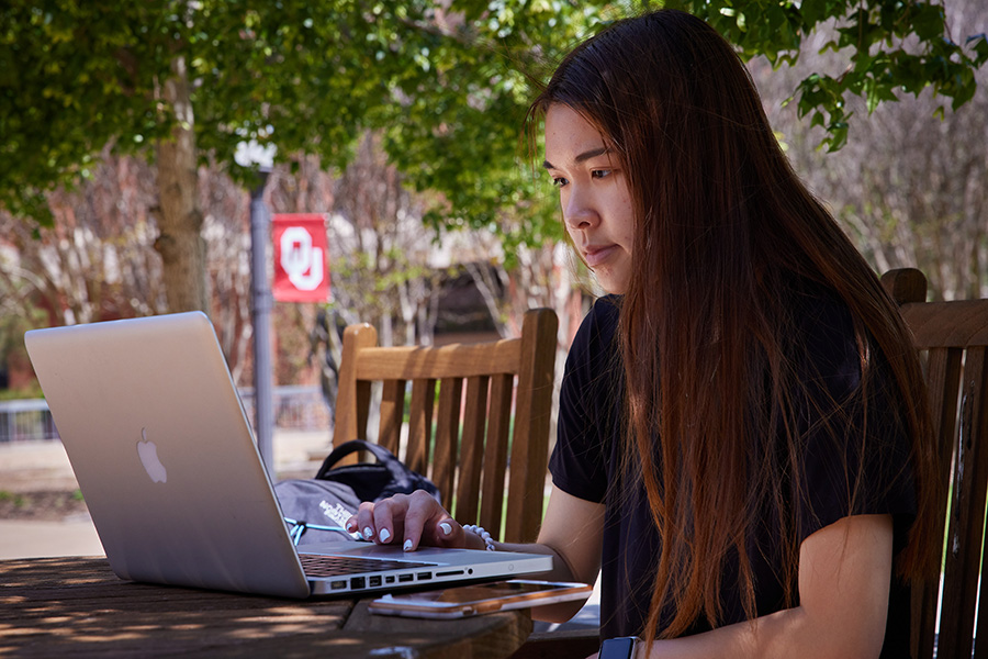 A student sitting outside on campus working on a laptop computer.