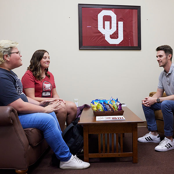 An advisor meeting with 2 students across a table. 