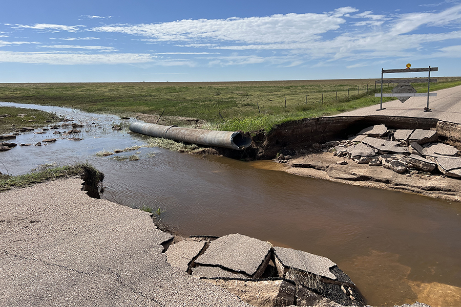 A muddy stream of water from a flash flood dividing a collapsed roadway.