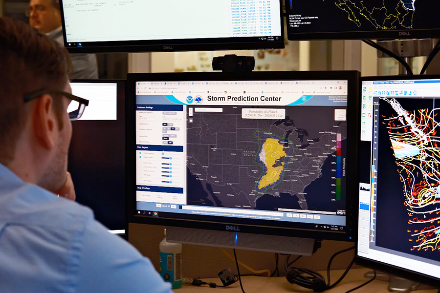 A scientist reviews several computer monitors displaying different radar information and weather data.