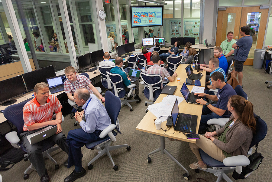 A group of forecasters in a large room with tables and computers.