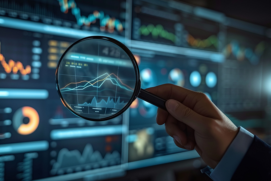 Image of hand holding a magnifying glass looking at a graphic with charts and statistics.