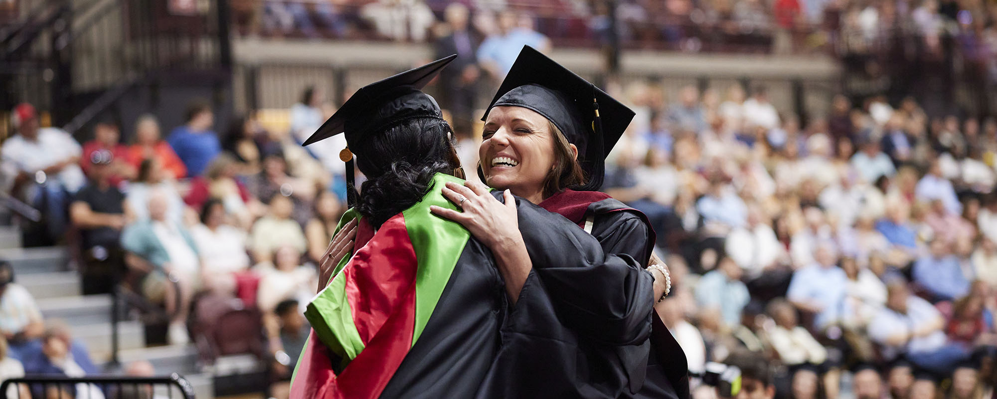 Two people in regalia embracing at a commencement celebration.