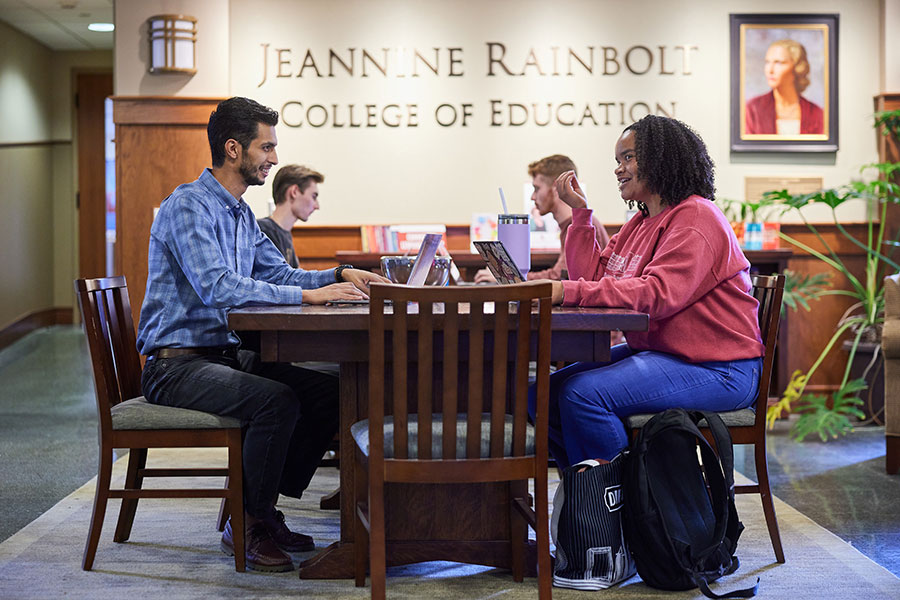 A group of graduate students work together on laptops at a table in the Rainbolt College of Education.