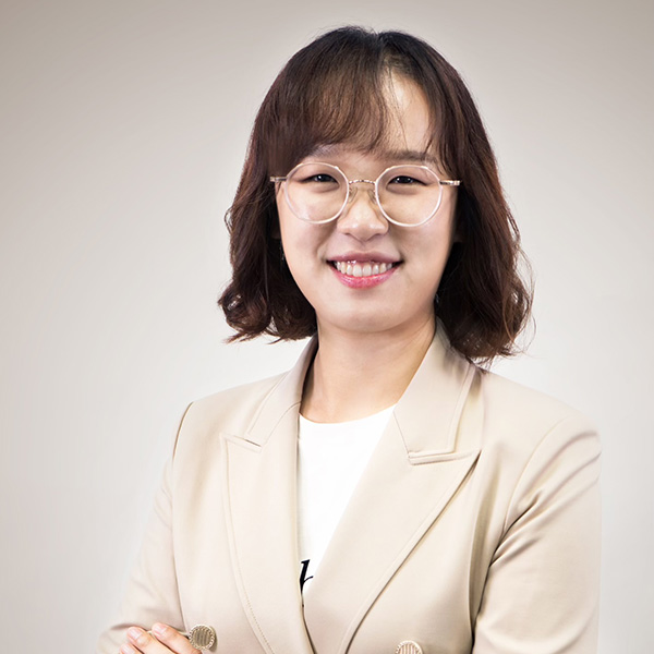 Woman in tan blazer and glasses with brown hair smiling