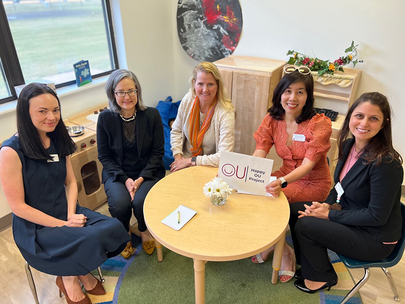 Five women sitting around a children's table looking up at the camera