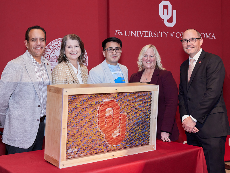 Two women and three men standing in front of a display made of pencils with the OU logo in the center