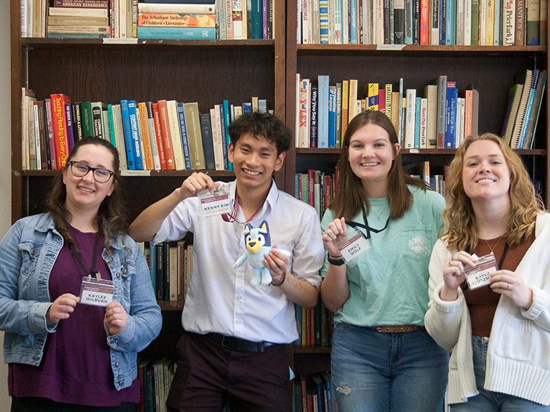 Three women and one man standing in front of a book case holding up their conference badges