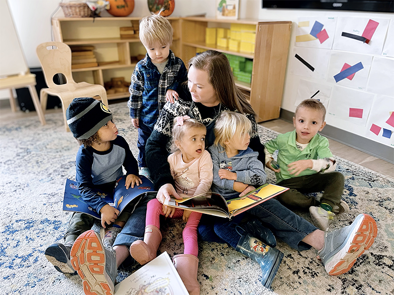 A woman is sitting on the floor reading a book, surrounded by children