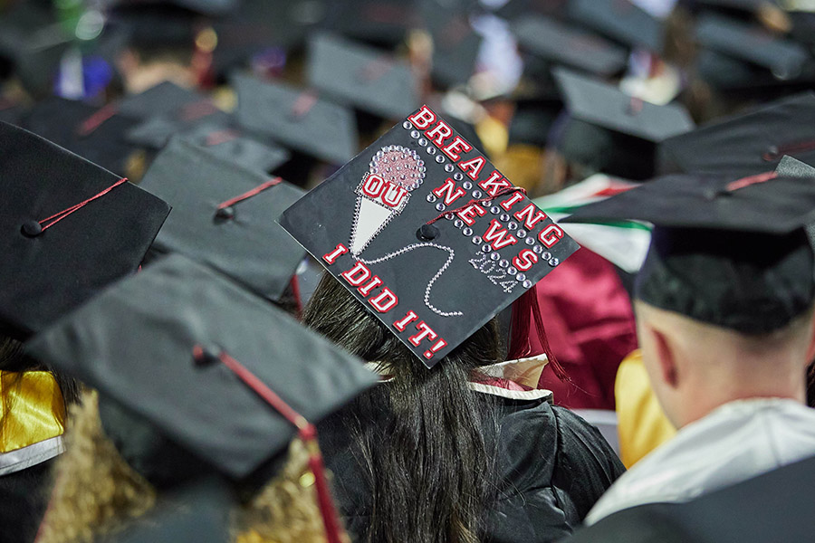 Graduates sitting in a crowd during the Gaylord College Commencement ceremony on May 10, 2024. Graduate decorated their cap to read "Breaking News, I did it!"
