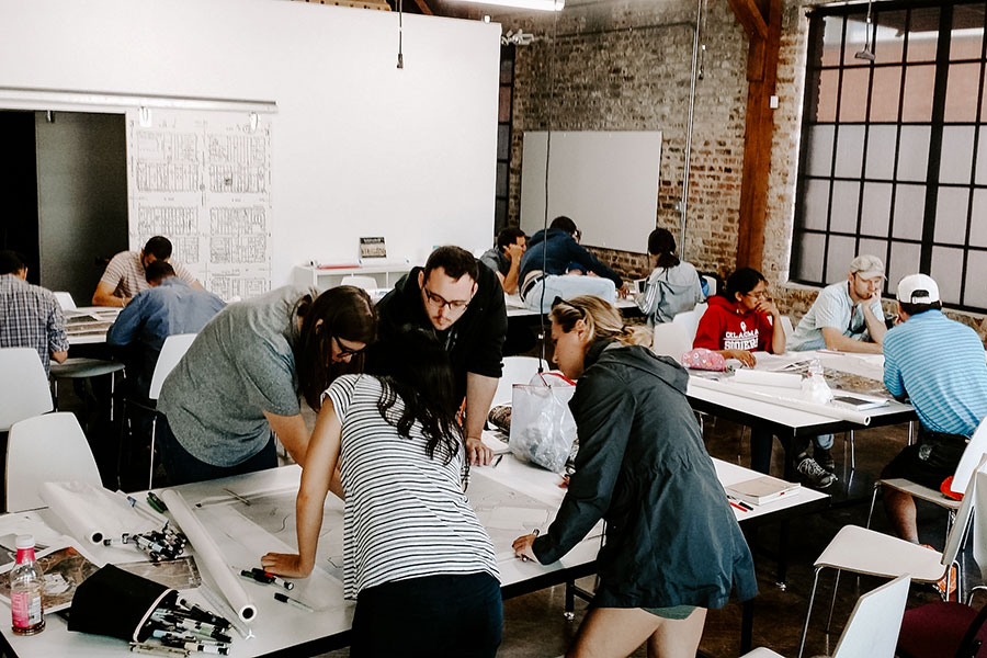 People standing around tables, working on architectural plans.