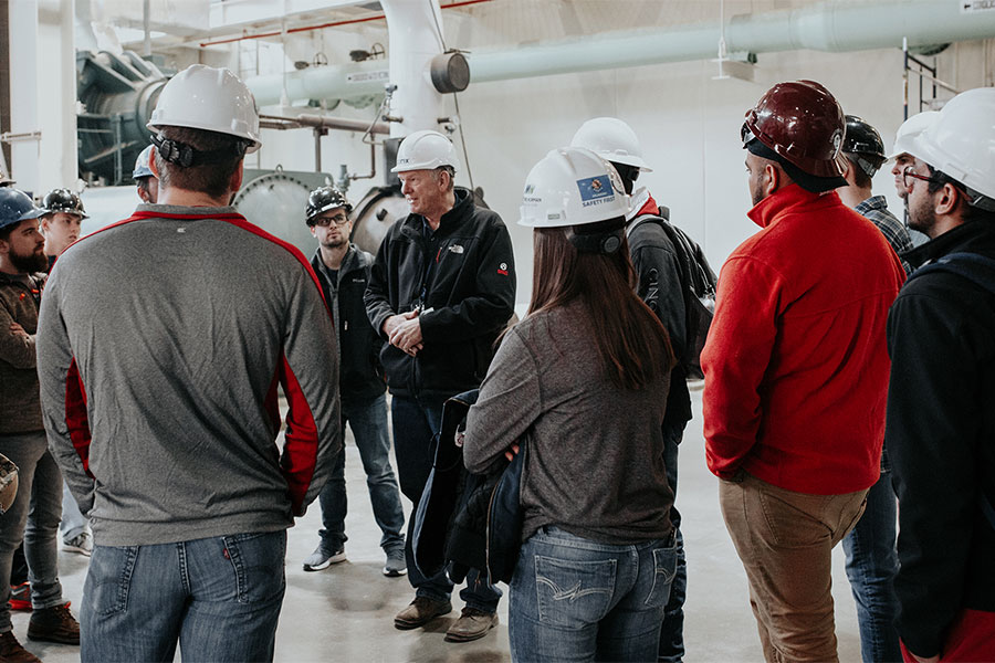 Students in hard hats, listening to a lecture.