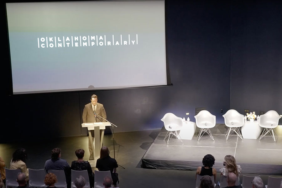 The opening program of Outré West, with a person standing on stage at a podium.