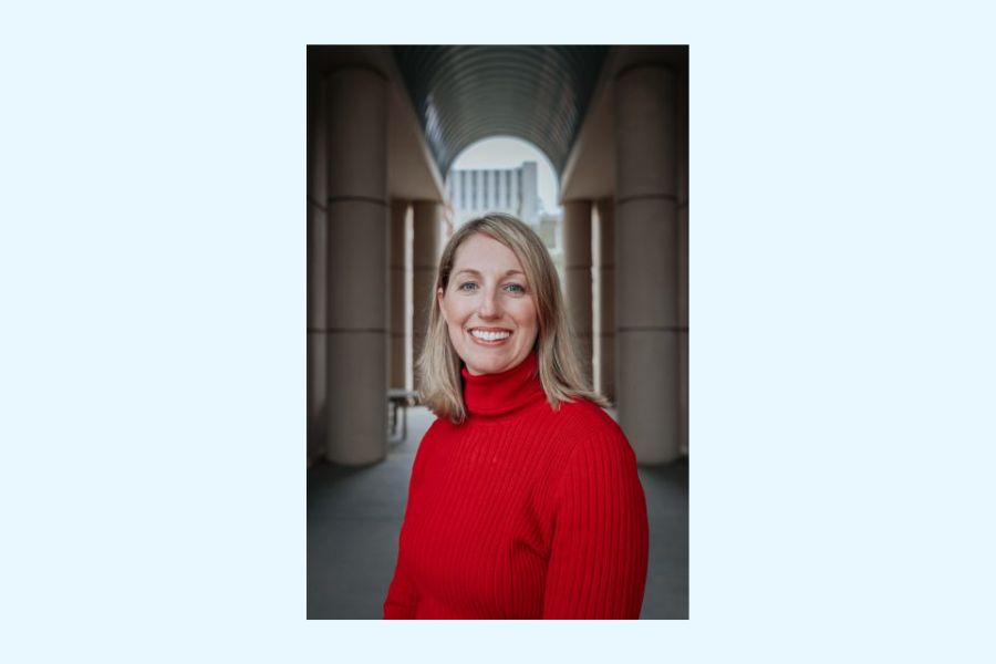 Headshot of a woman in a red long sleeve turtle neck top with an arch in the background