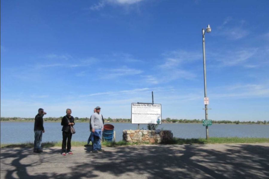 Individuals standing on a sidewalk above a reservoir with water in the back