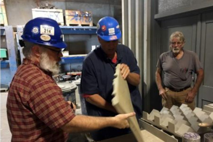 Three men standing, two with hard hards, examining some sort of material in a lab