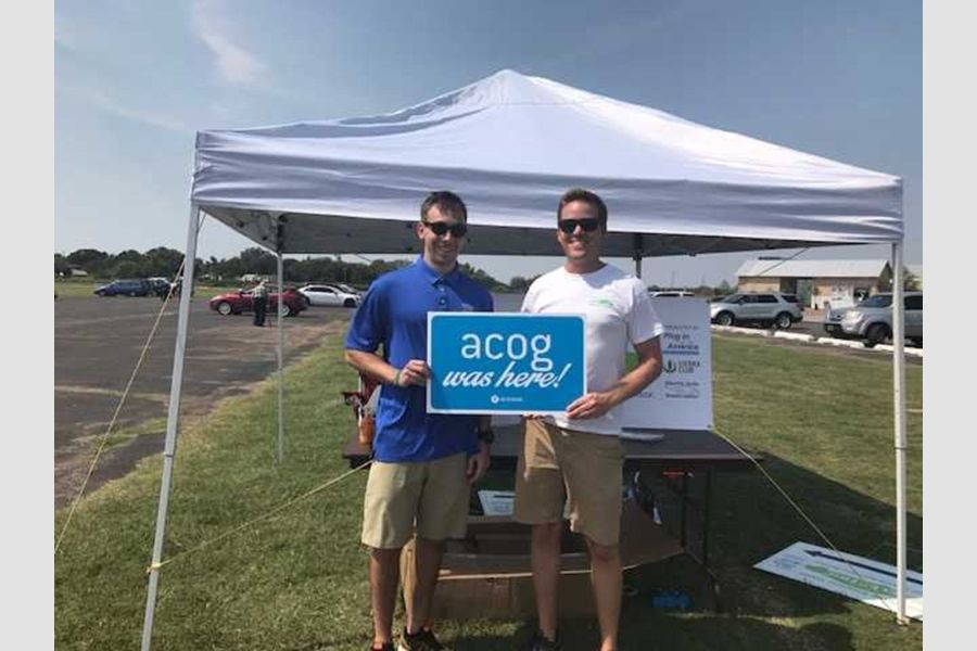 Matthew McClure and colleague at an outdoor event with a sign that says A C O G was here.