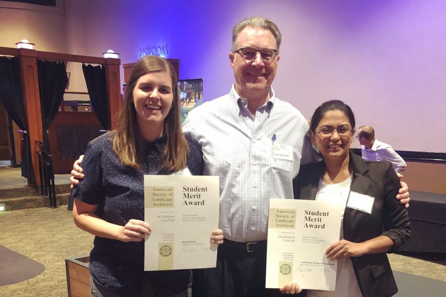 An older gentleman standing between two younger women holding awards in a conference center