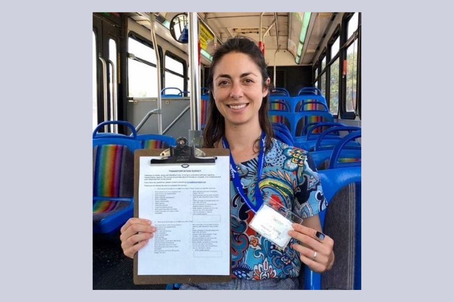 Student on a bus holding a clipboard and a badge and smiling for a photo