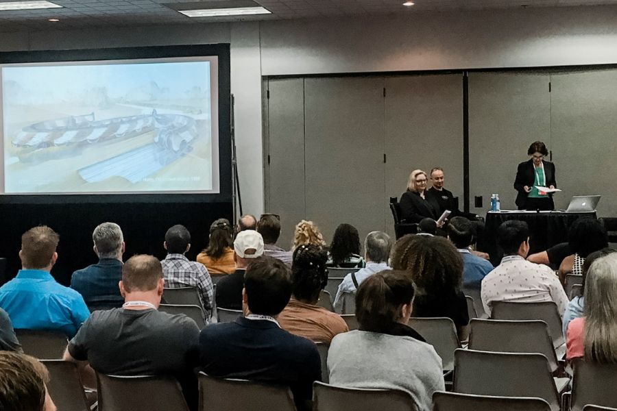 Individuals standing on a podium with a large projection on a screen presenting to an audience