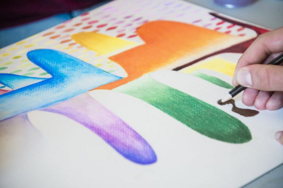 A hand with a pencil coloring on a paper with waves of differnet colors